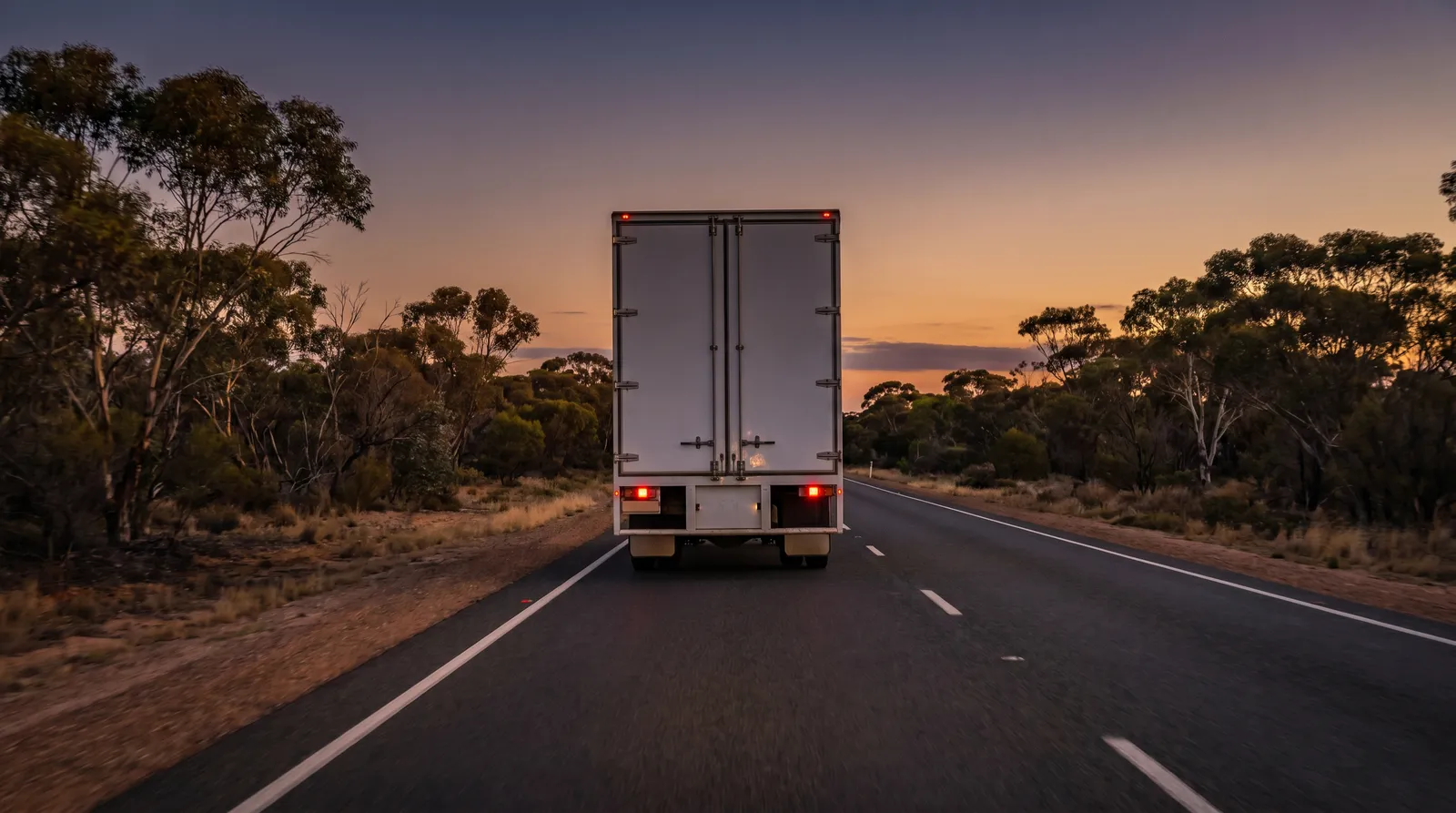 A plain white moving truck on a highway through eucalypt country at dusk
